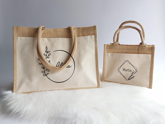 personalisierte Jutetaschen in verschiedenen Größen und Designs.Links Großer Shopper mit Vordertasche und schwarzem Aufrduck Ringdesign 1. rechts kleine Jutetasche mit Vordertasche und Ringdesign 2. Tolles Geschenk für Hebammen und Erzieherinnen